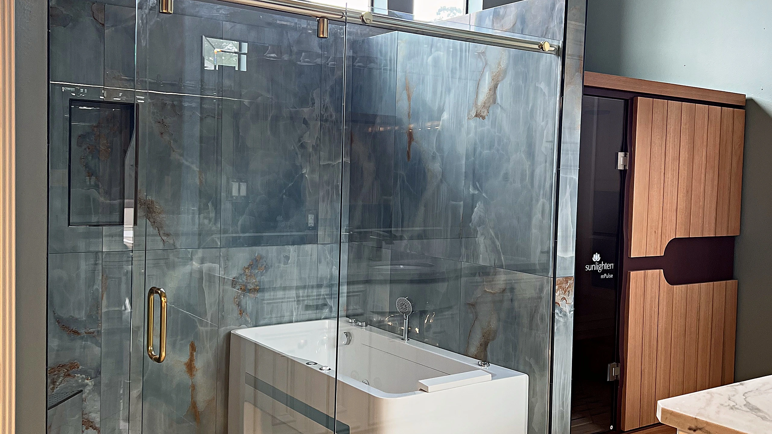 Finished master bathroom renovation in Bunker Hill Village featuring natural stone surfaces, a frameless glass shower, and warm metal finishes