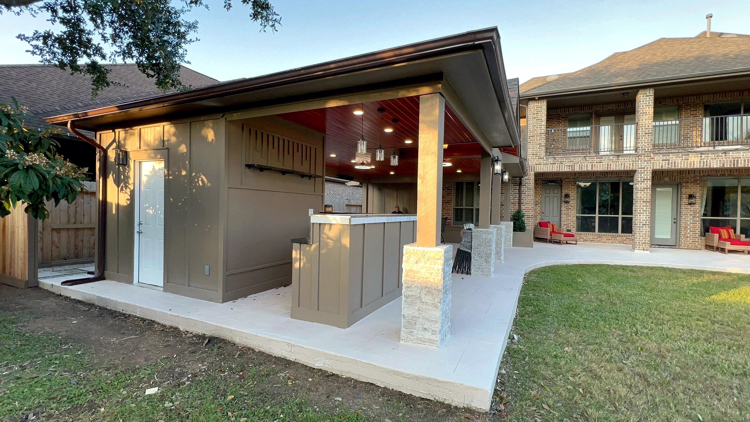 Side elevation of outdoor pavilion addition with board-and-batten utility room, stone-clad bar counter, and wood ceiling