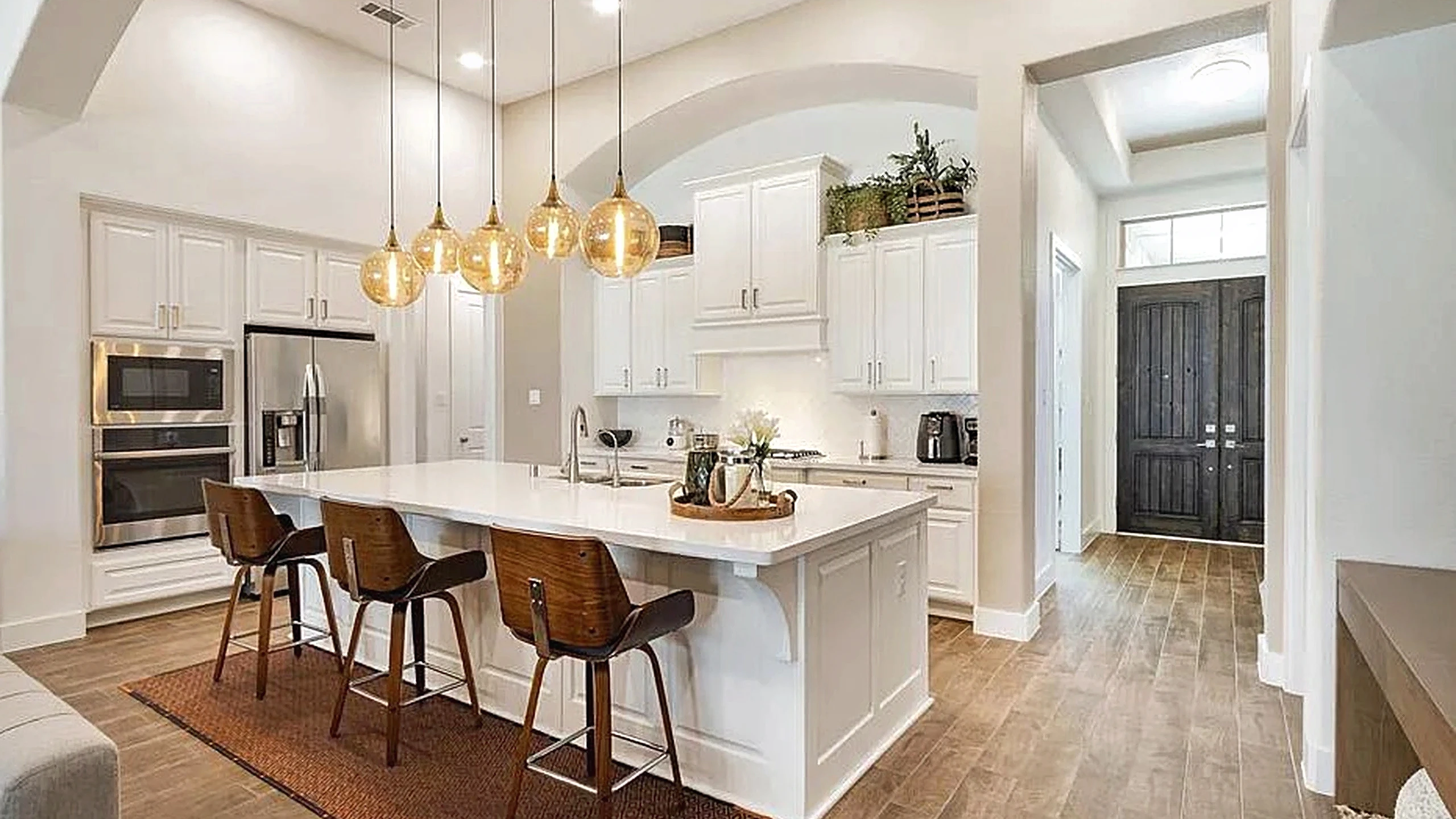Cypress kitchen remodel with a white island and bar stools, white cabinetry, wood-look flooring, and pendant lights above the island