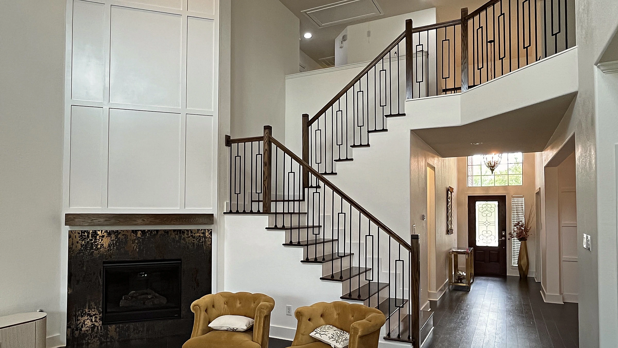 Two-story living room with white board-and-batten fireplace wall, dark hardwood floors, and open stair with iron balusters