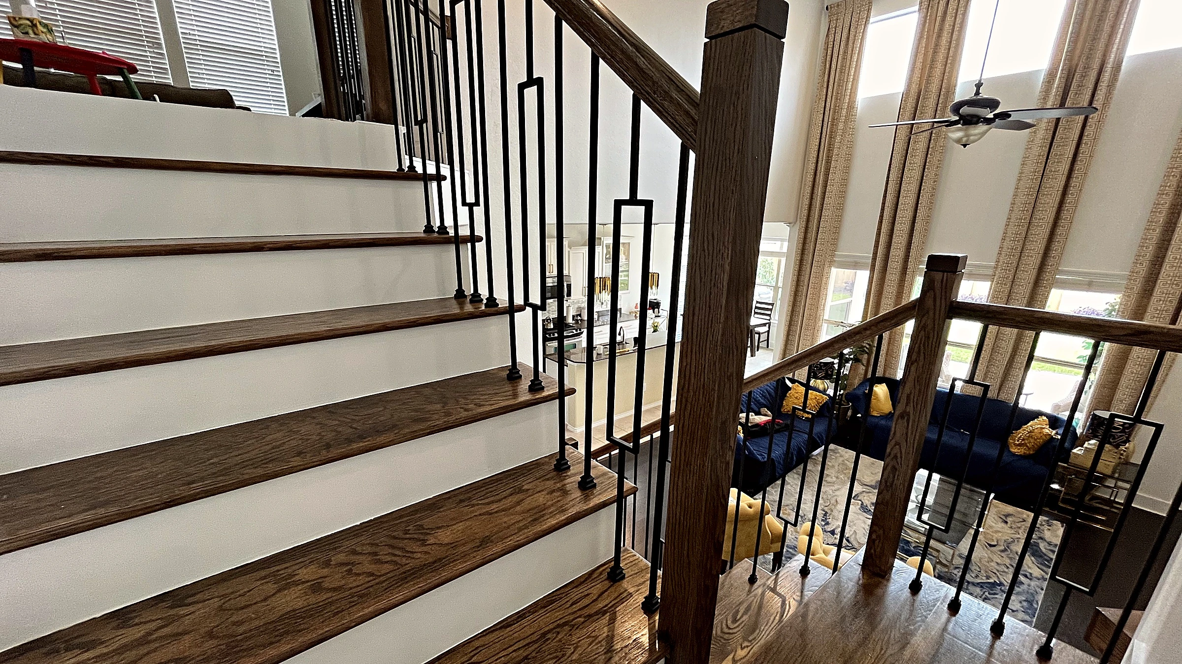 Dark-stained wood stair treads and painted risers with rectangular-loop iron balusters and wood newel post in a Fulshear home remodel