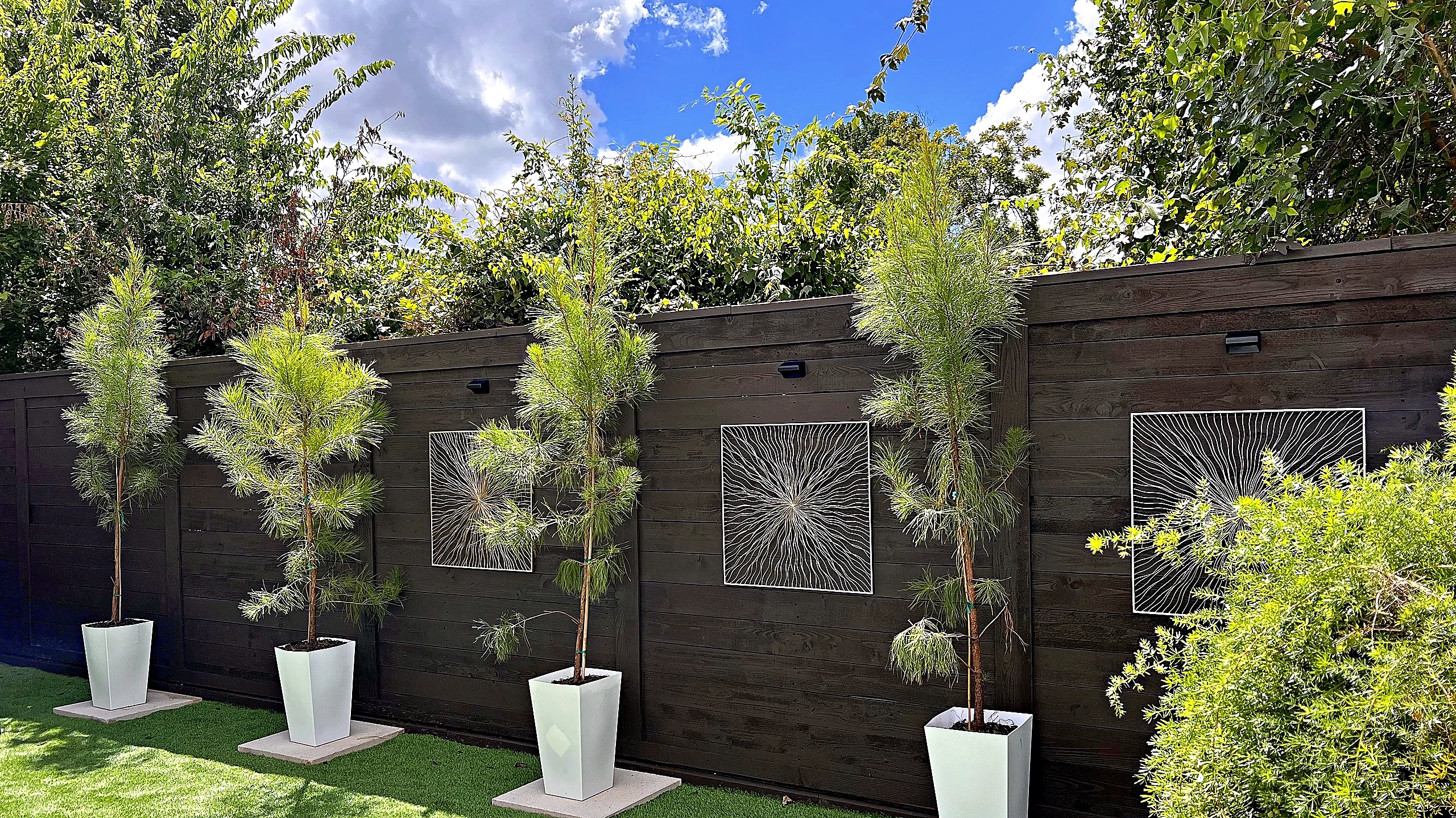 Spring Valley Village townhouse courtyard with potted plants along a dark wood fence with decorative panels, Houston