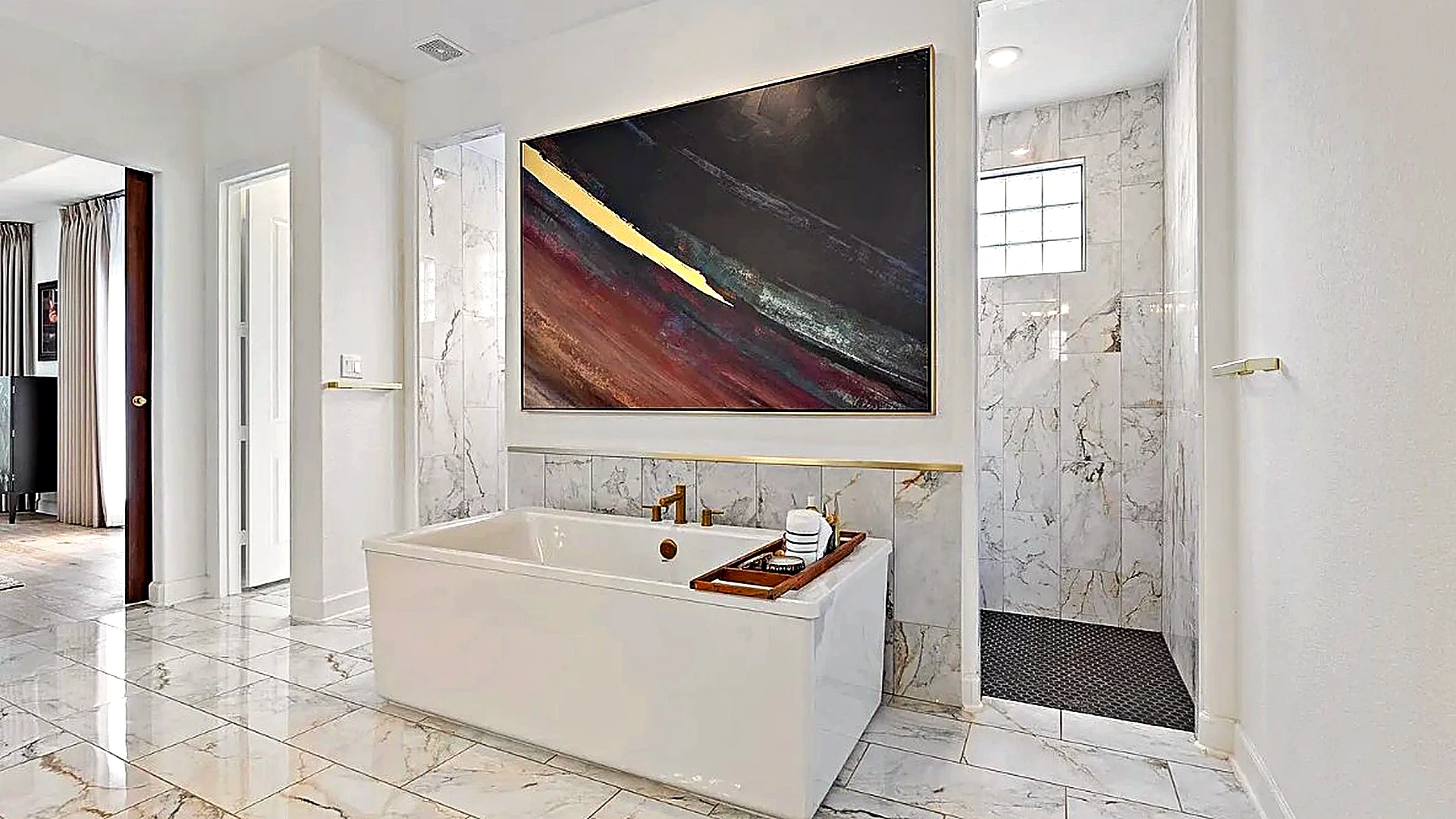 Freestanding white soaking tub, brass hardware, veined stone walls, and abstract canvas in a primary bathroom remodel, The Woodlands
