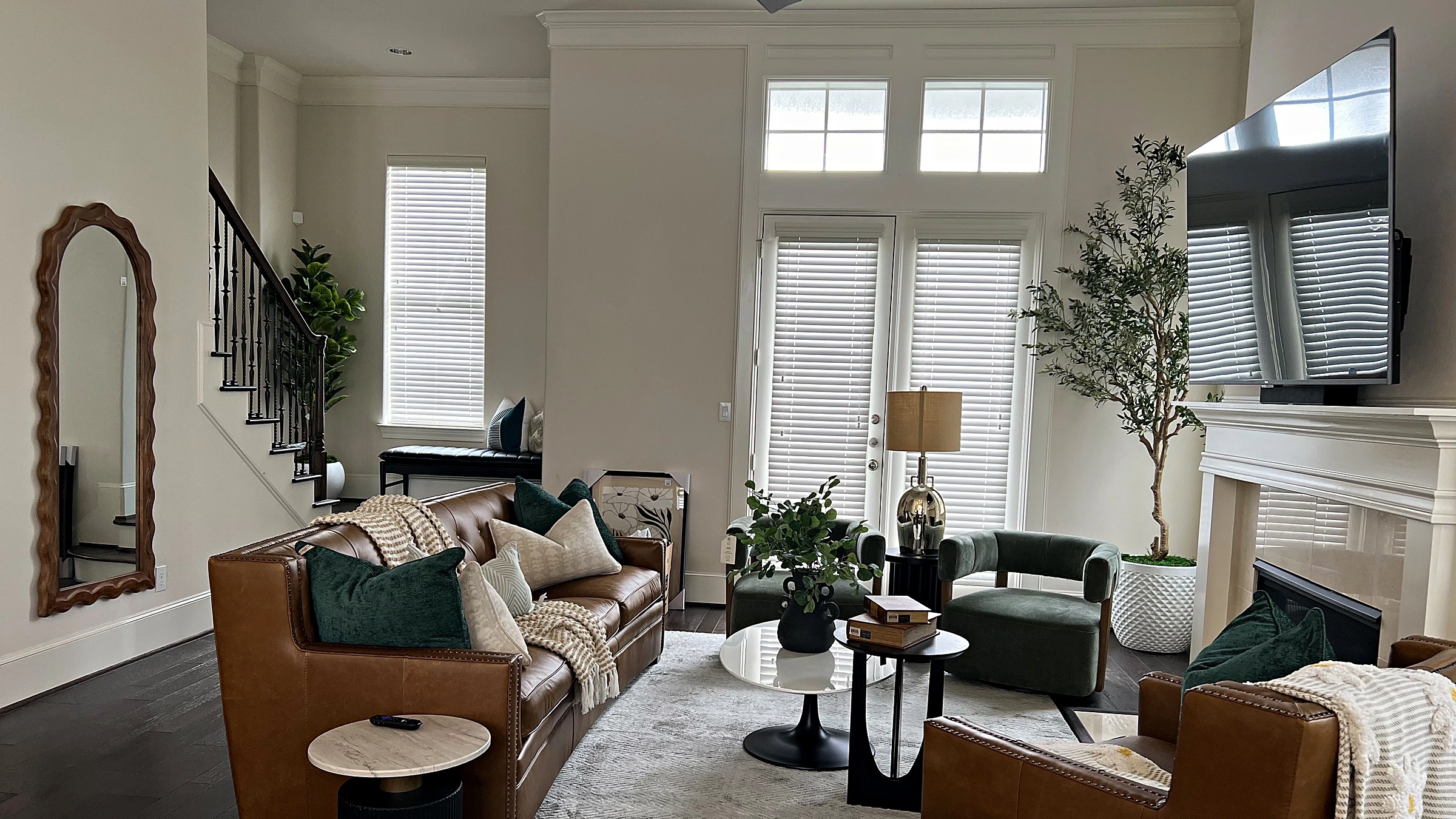 Living room in a West University Place townhome with a brown leather sofa, fireplace, a framed mirror, and blinds at the windows
