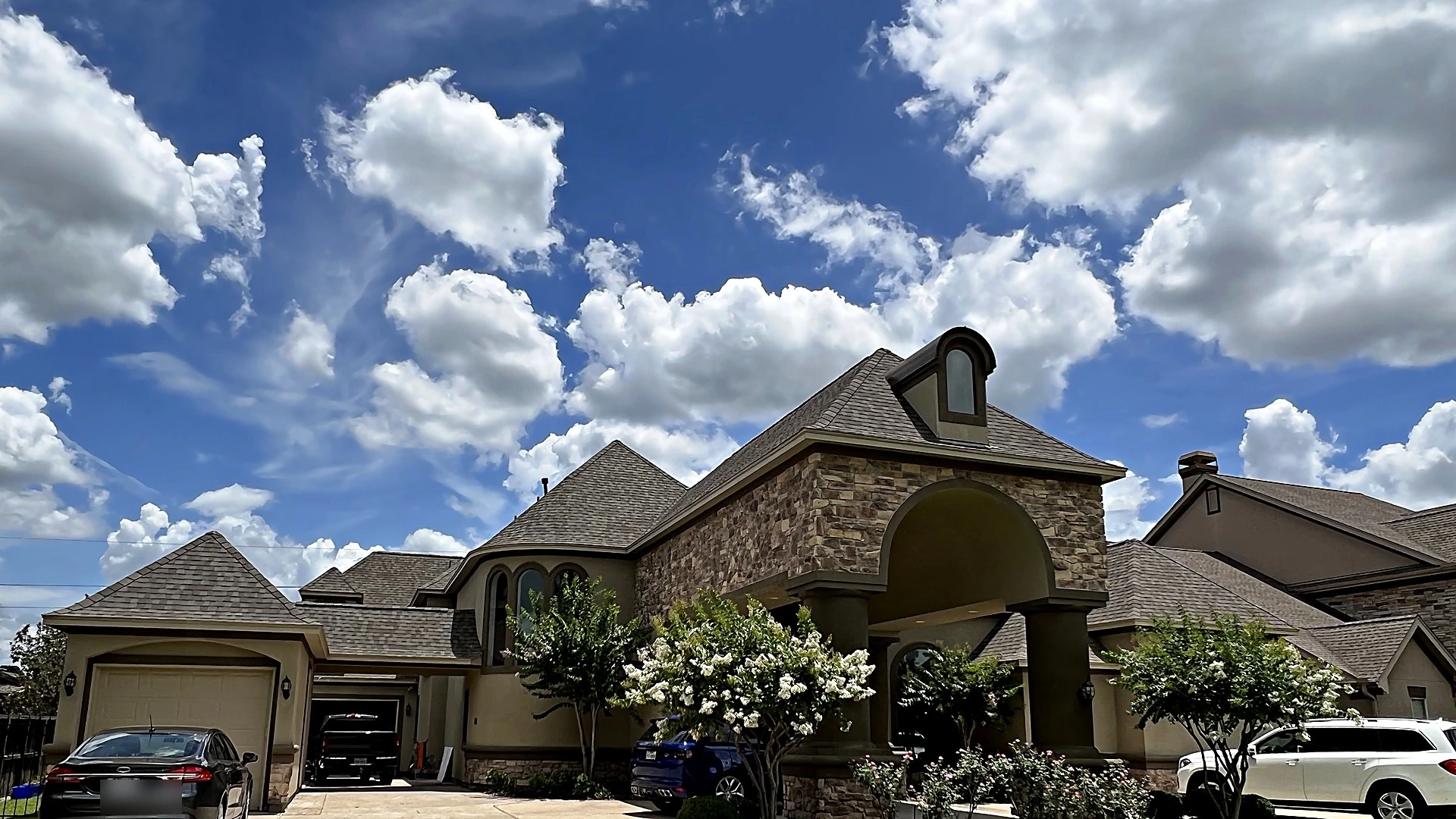 Multi-gable shingle roof on a stone and stucco home under a blue Texas sky, roofing by Bager in Houston, TX